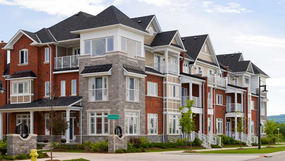 A row of modern three-story townhouses featuring a mix of red brick and grey stone facades, white balconies, and multiple gabled roofs - labonteins.com