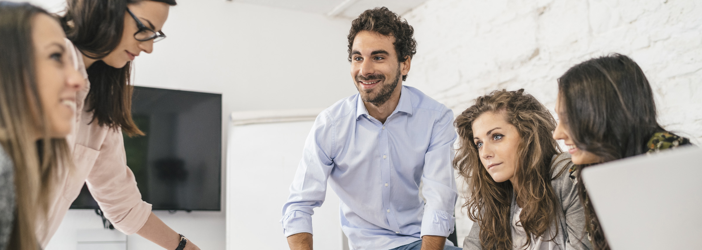 A diverse group of young professionals collaborates in a bright office, gathered around a workspace with engaged and positive expressions -labonteins.com