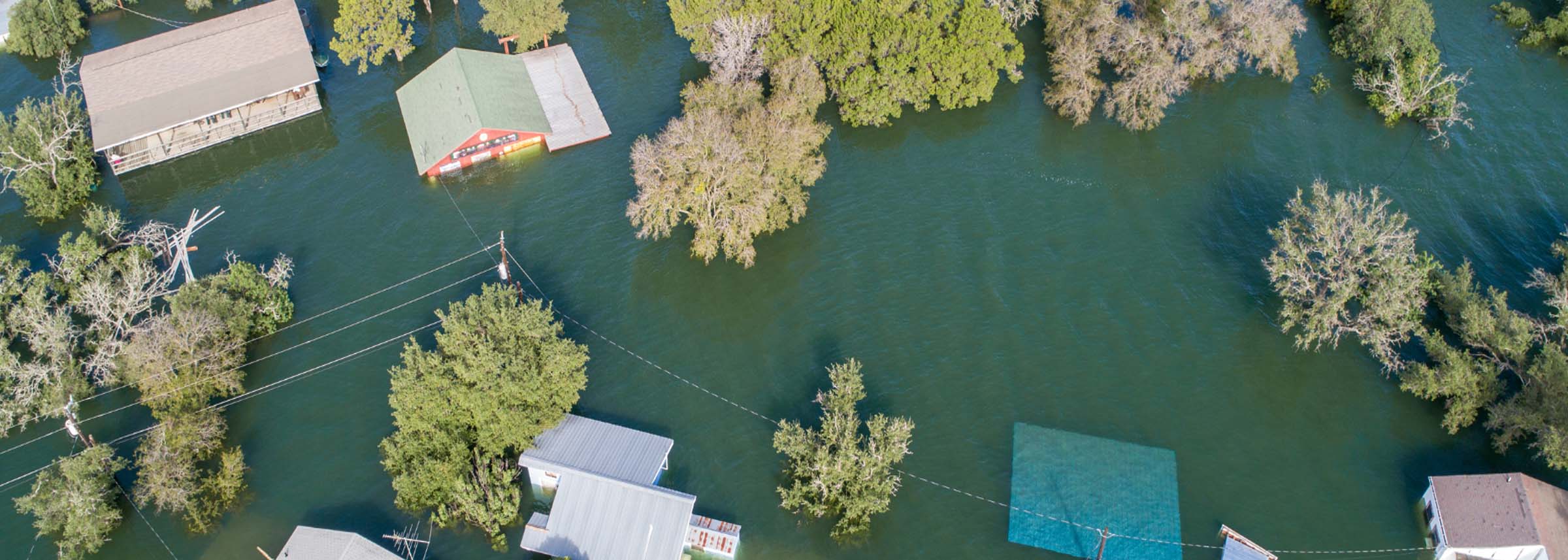 An aerial view of significant flooding in a residential or recreational area, with multiple buildings and trees partially submerged in dark green water -labonteins.com